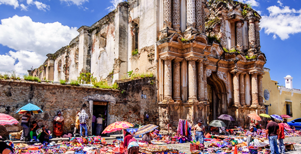 Antigua, Guatemala - October 4, 2014: Local, Mayan men & women sell handmade textiles & handicrafts to tourists at weekend market in cobblestone street outside El Carmen ruins in colonial city & UNESCO World Heritage Site of Antigua.